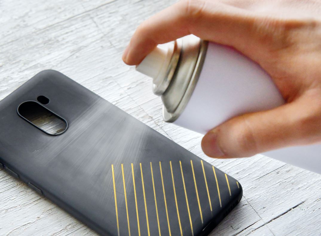 A smartphone case embellished with golden stripes getting sprayed on with a spray can.